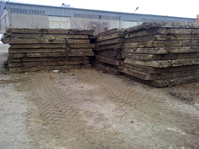 Dwa stosy używanych, betonowych płyt na ziemi z widocznymi śladami opon, w tle budynek przemysłowy.